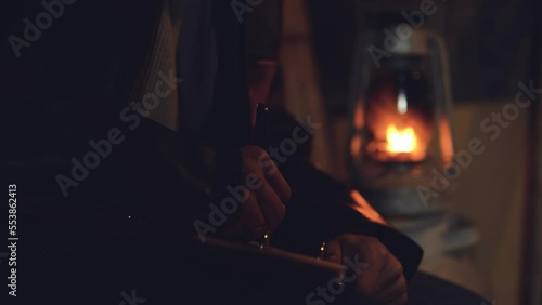 Adult seriously man with beard write old diary wear a vintage leather jacket in retro small fishing house of wood at deep night. Vintage a kerosene lamp fire photo