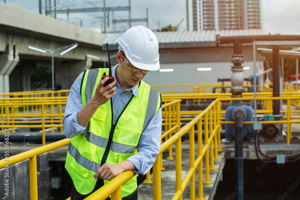 Young engineer wearing safety uniform used radio communication checking the wastewater treatment pond industry. Young engineer wearing safety uniform used radio communication checking the wastewater treatment pond industry.