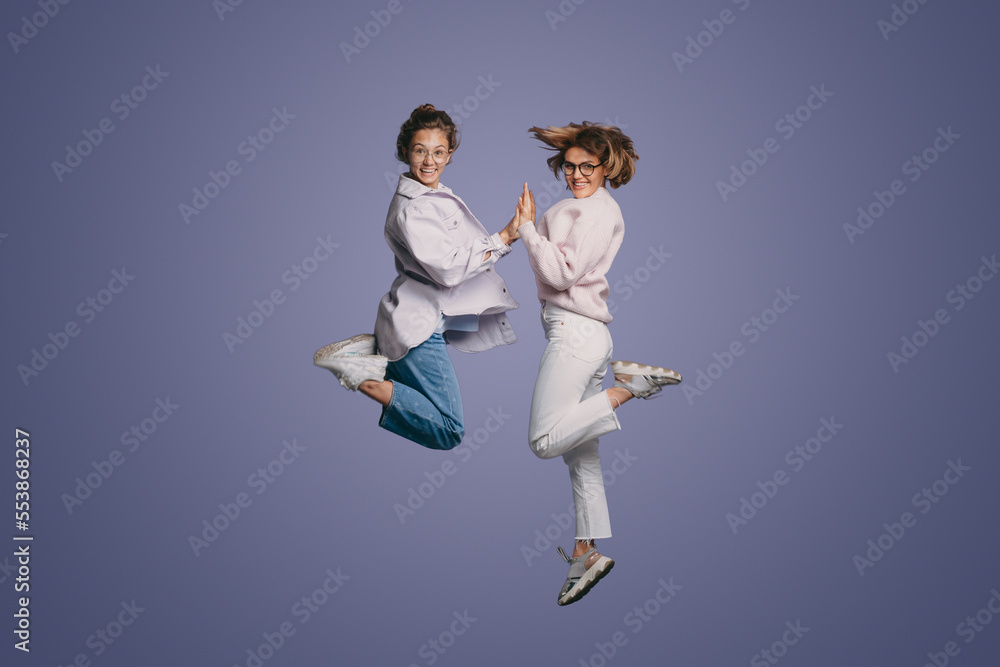 Young cute excited funny smiling women wearing casual clothes jumping up in air and high five clapping hands with joy isolated over purple background. Young cute excited funny smiling women wearing casual clothes jumping up in air and high five clapping hands with joy isolated over purple background.