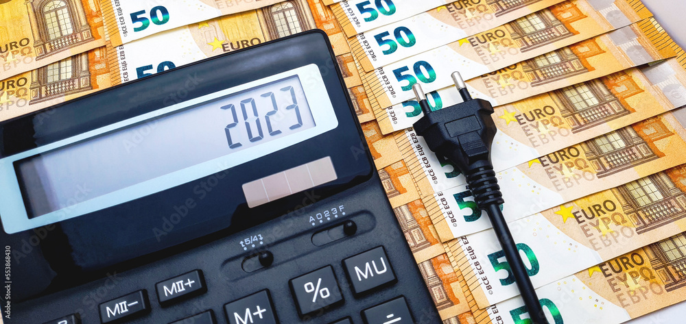 Calculator, electric plug, 50 euro notes and coins in the background. The concept of the high cost of electricity, rising inflation and the impending crisis in 2023