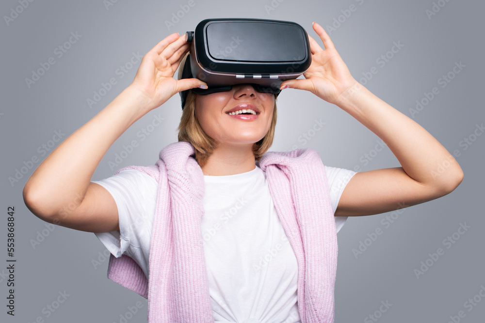 Portrait of a charming woman wearing VR glasses on an gray background. Innovative technologies. Game industry. Mixed media Portrait of a charming woman wearing VR glasses on an gray background. Innovative technologies. Game industry. Mixed media
