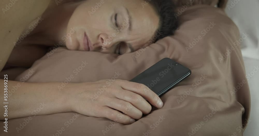 Woman with digital addiction. A view of a woman with device addiction sleep in the bed with her smartphone in the room. Woman with digital addiction. A view of a woman with device addiction sleep in the bed with her smartphone in the room.