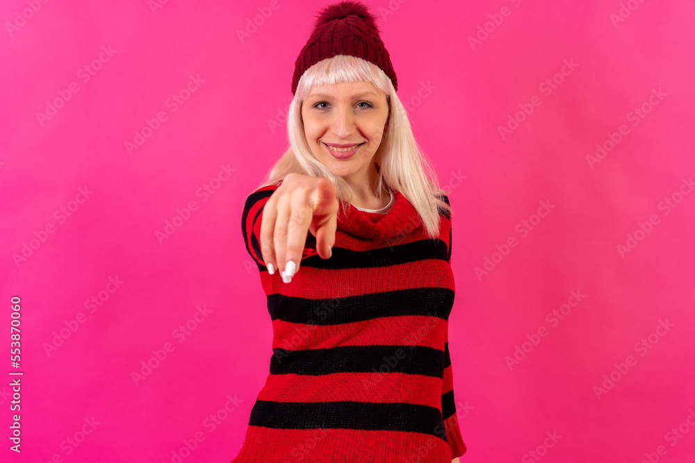 Blonde caucasian girl on pink background studio, winter theme, smiling pointing Blonde caucasian girl on pink background studio, winter theme, smiling pointing