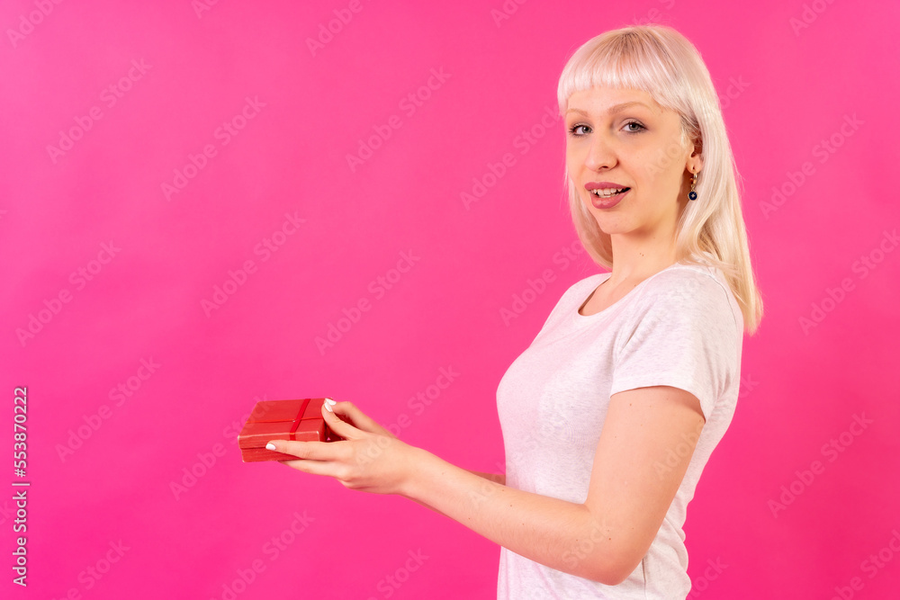 Handing a gift to the left, Blonde Caucasian girl in pink background studio Handing a gift to the left, Blonde Caucasian girl in pink background studio