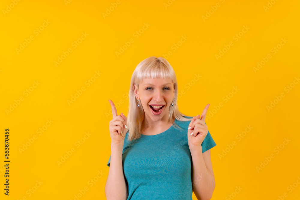 Portrait smiling pointing up, blond caucasian girl in studio on yellow background Portrait smiling pointing up, blond caucasian girl in studio on yellow background