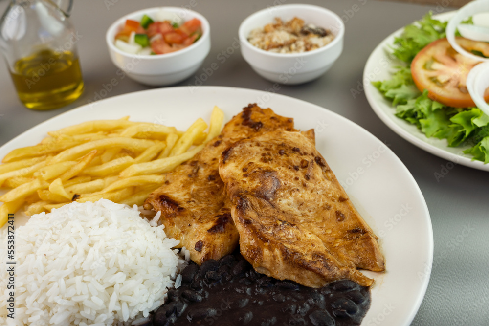 Delicious executive dish of chicken fillet, rice, beans, french fries and green salad with lettuce, tomato and onion accompanied by farofa and vinaigrette. Typical Brazilian food. Selective focus Delicious executive dish of chicken fillet, rice, beans, french fries and green salad with lettuce, tomato and onion accompanied by farofa and vinaigrette. Typical Brazilian food. Selective focus
