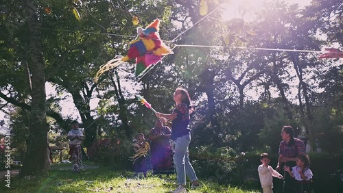 Familia indigena celebrando un cumpleaños con piñata en el parque. Joven adolecente quebrando una piñata.  photo