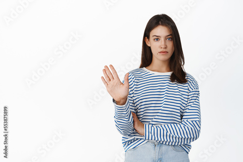 Image of serious reluctant girl rejecting, waving hand to give negative answer, refusing, being unamused of offer, standing against white background