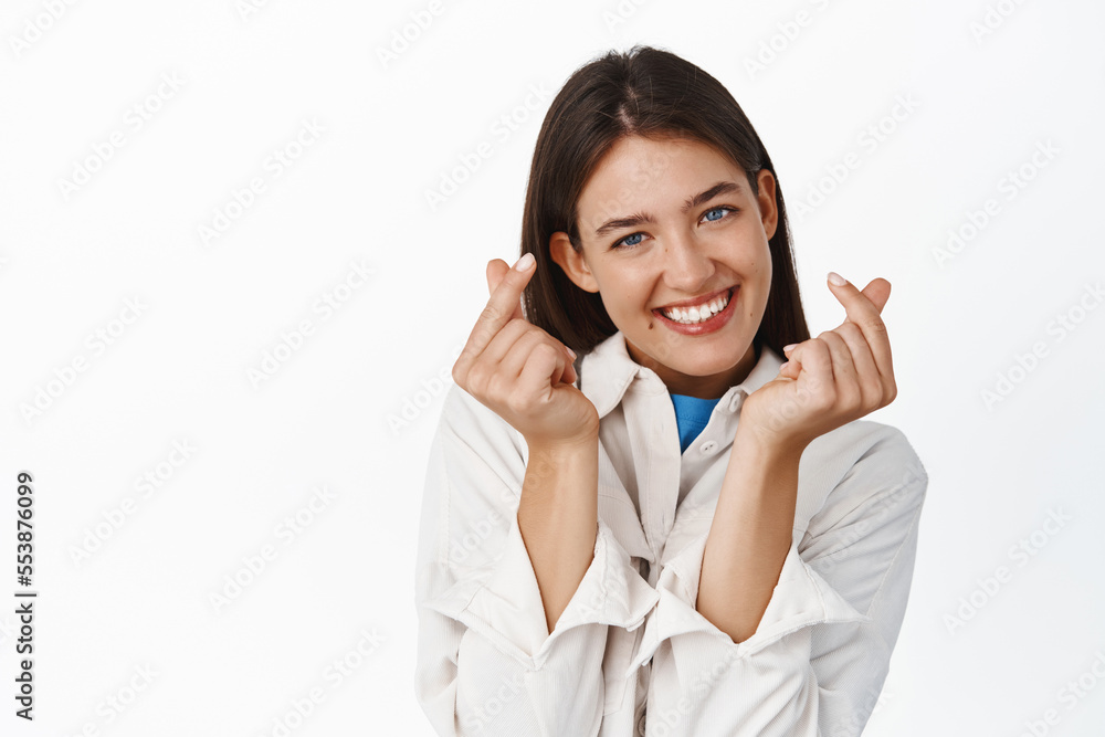 Cute smiling girl showing hand hearts and looking romantic at camera, standing over white background Cute smiling girl showing hand hearts and looking romantic at camera, standing over white background