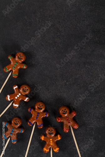 Christmas cookie in the form of a gingerbread man, covered with colored icing sugar, on a wooden stick. Dark gray background. Top view. Copy space