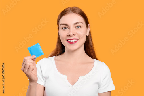 Woman holding condom on yellow background. Safe sex