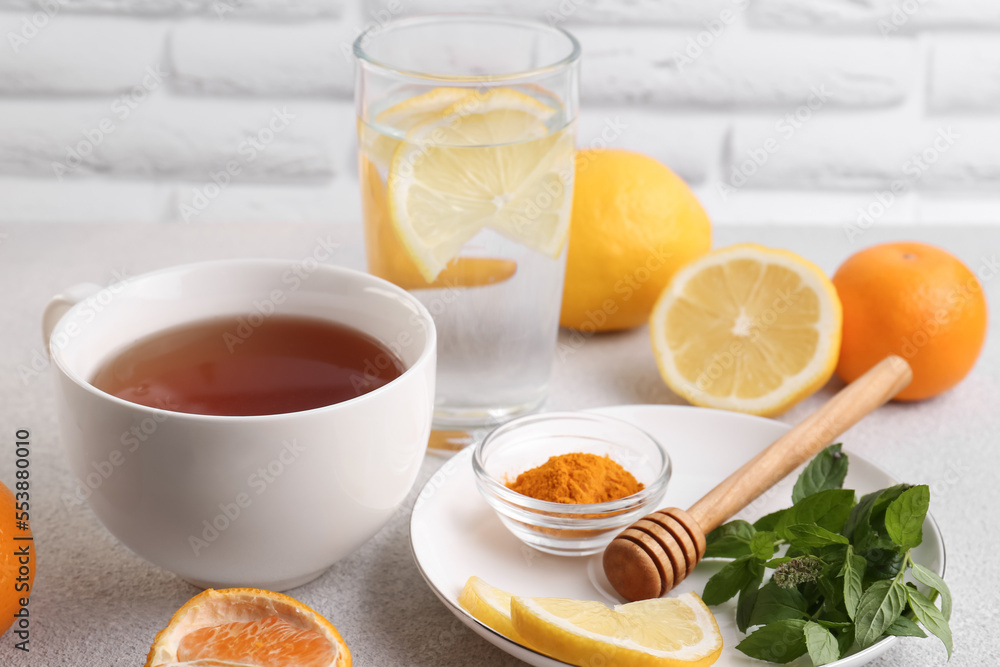 Cup of delicious immunity boosting tea with citrus fruits and turmeric on light grey table Cup of delicious immunity boosting tea with citrus fruits and turmeric on light grey table