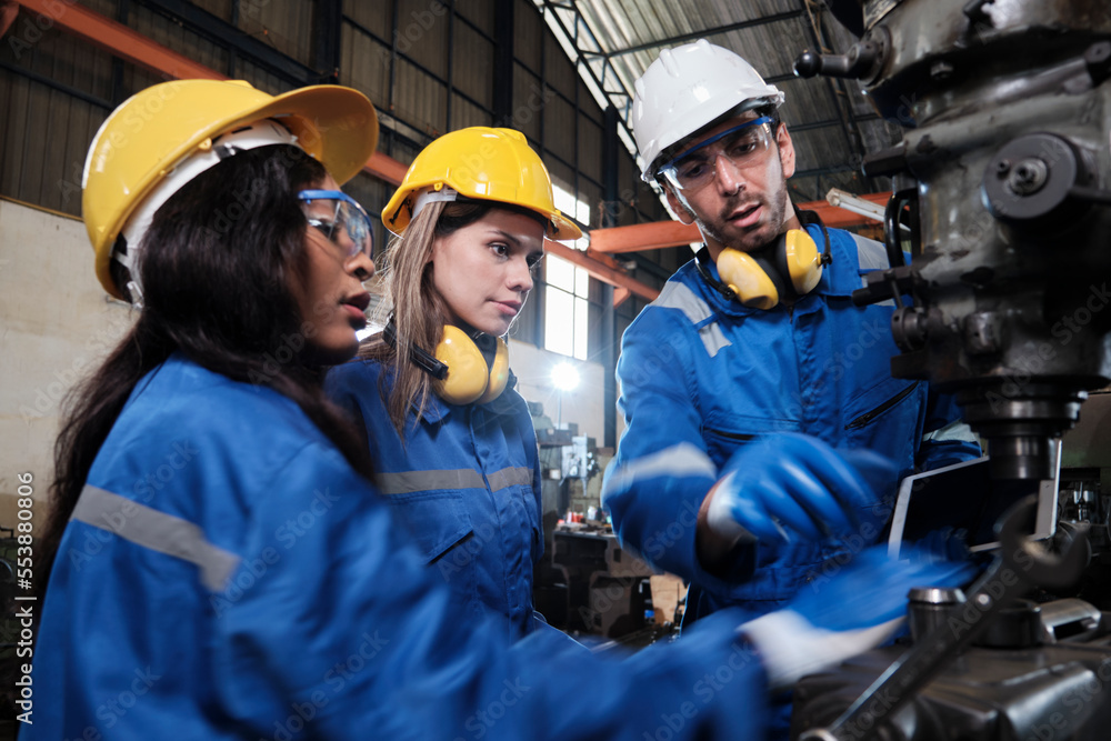 Fototapeta premium An Industrial workers team in protective and safety uniforms and hardhats, male manager, and female colleagues work with metalwork machines in manufacturing factory. Professional production engineer.