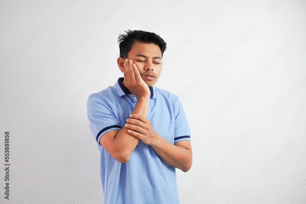 Tooth ache. Young asian man feeling pain, holding his cheek with both hands, suffering from bad toothache, having painful expression wearing blue t shirt isolated on white background Tooth ache. Young asian man feeling pain, holding his cheek with both hands, suffering from bad toothache, having painful expression wearing blue t shirt isolated on white background