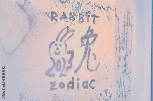 New Year's drawing on a frozen window. The hieroglyph of the rabbit is the zodiac symbol of the Chinese New Year 2023. Happy New Year and Merry Christmas. Frosty patterns on glass. Selective focus.