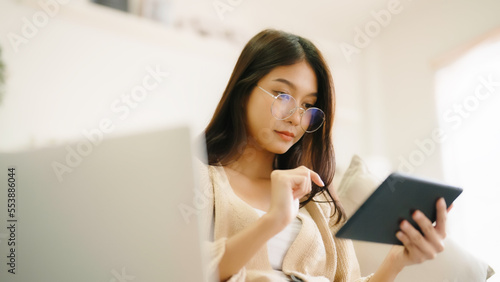 Young asian woman wearing glasses and using tablet while seated on couch at home