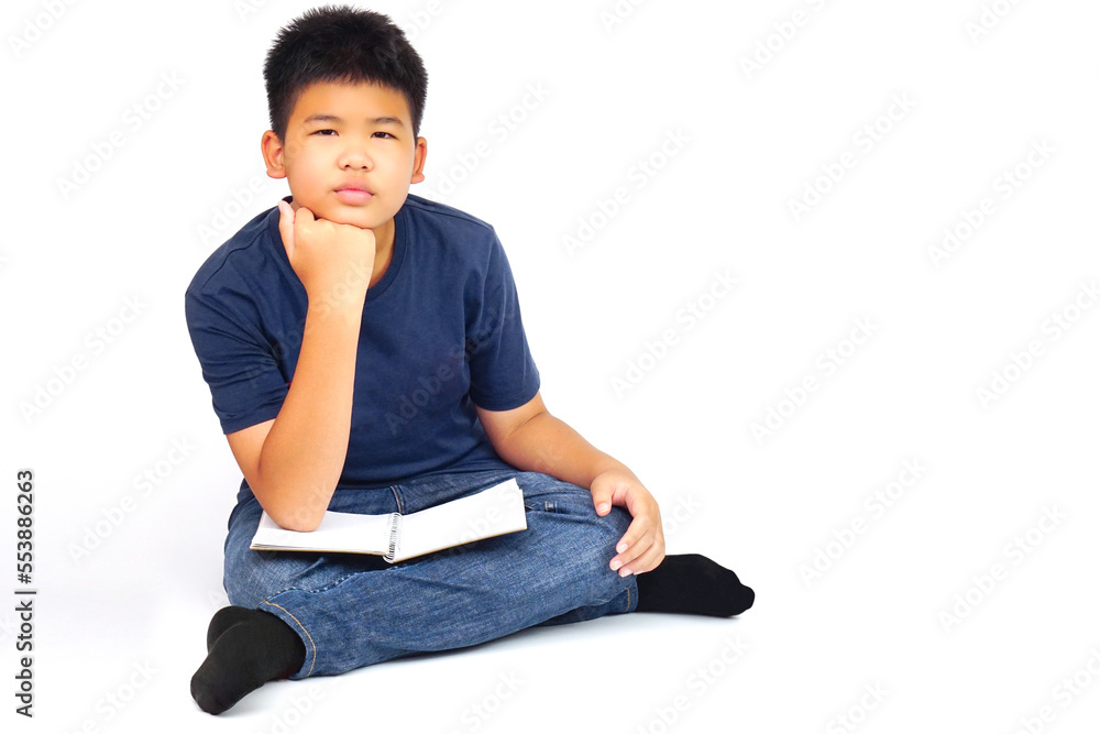 Young asian boy sitting cross-legged, with resting his chin on his hand and a book on his thigh. Education and learning concept.