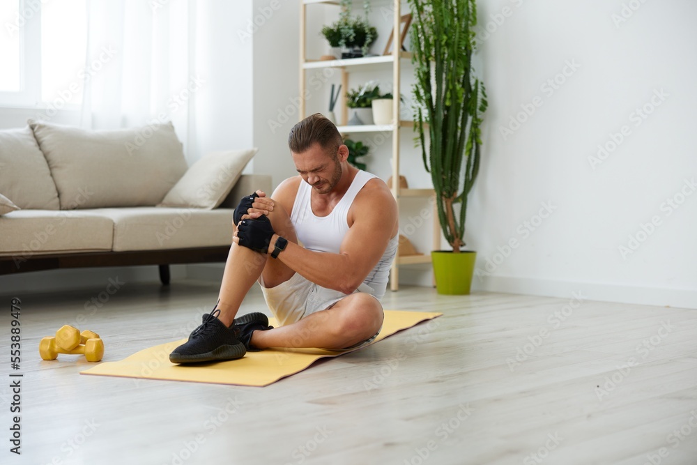 Man sports leg injury and pain, muscle and ligament sprain from exercise, pumped up man fitness trainer works out at home, the concept of health and body beauty Man sports leg injury and pain, muscle and ligament sprain from exercise, pumped up man fitness trainer works out at home, the concept of health and body beauty