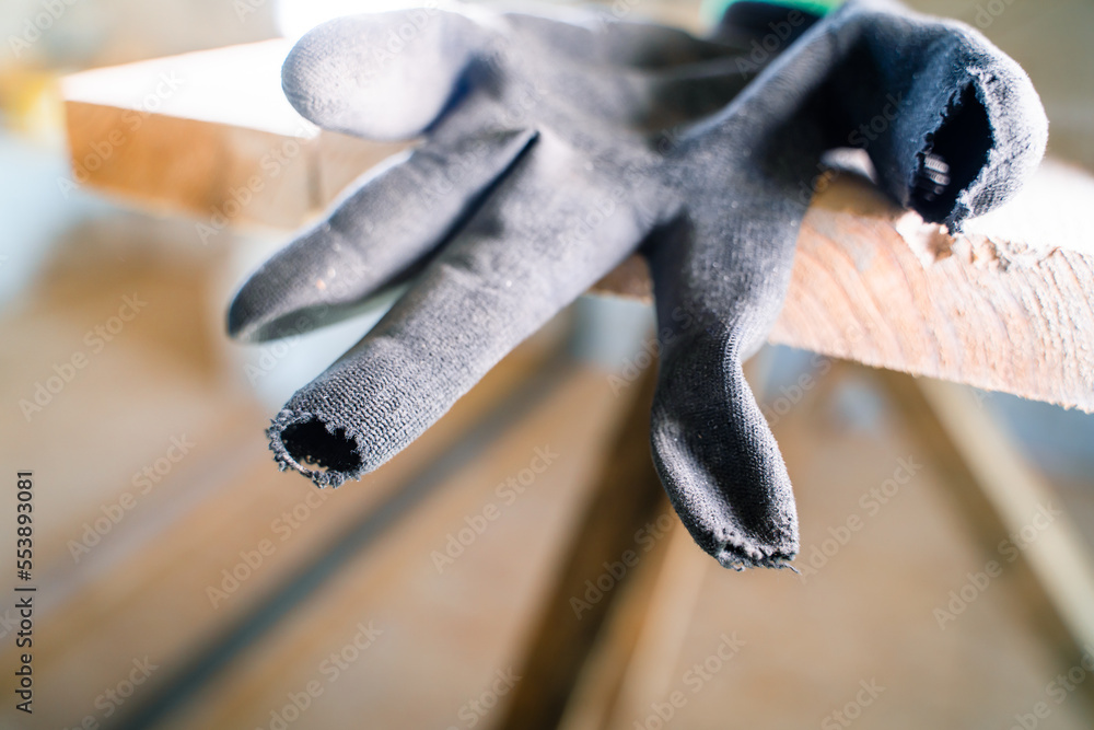 Foto Stock Black construction glove with rubbed fingers close-up. Holeful  work gloves at a construction site on wooden scaffolding. Poor quality protective  gloves torn at the fingers. Worn Builder's Equipment | Adobe