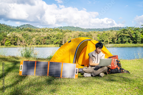 Young travel man relax and enjoy camping . Hand male plug in portable solar panel charging laptop computer by multipurpose cable, Clean energy for using in camping or at home when NO electricity photo