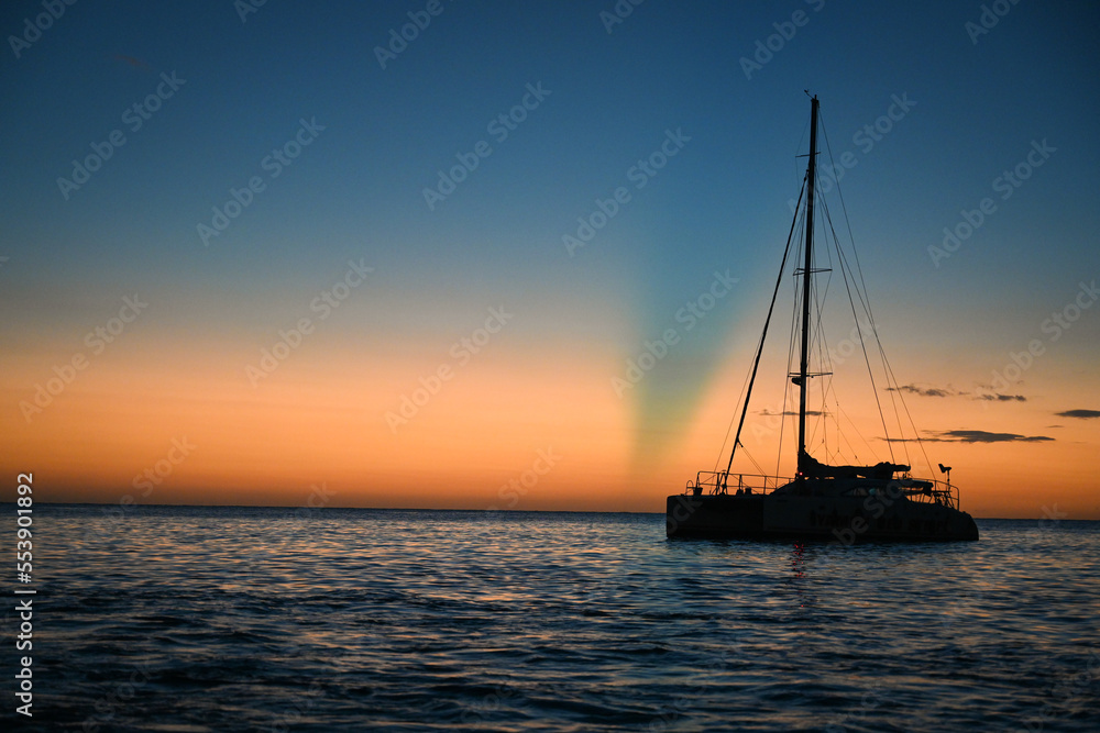 Sailboat in silhouette in front of a sunset on the Caribbean Ocean in Jamaica, Negril - orange, blue