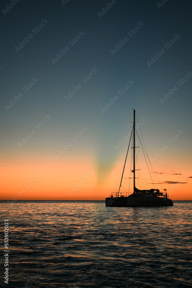 Sailboat in silhouette in front of a sunset on the Caribbean Ocean in Jamaica, Negril - orange, blue