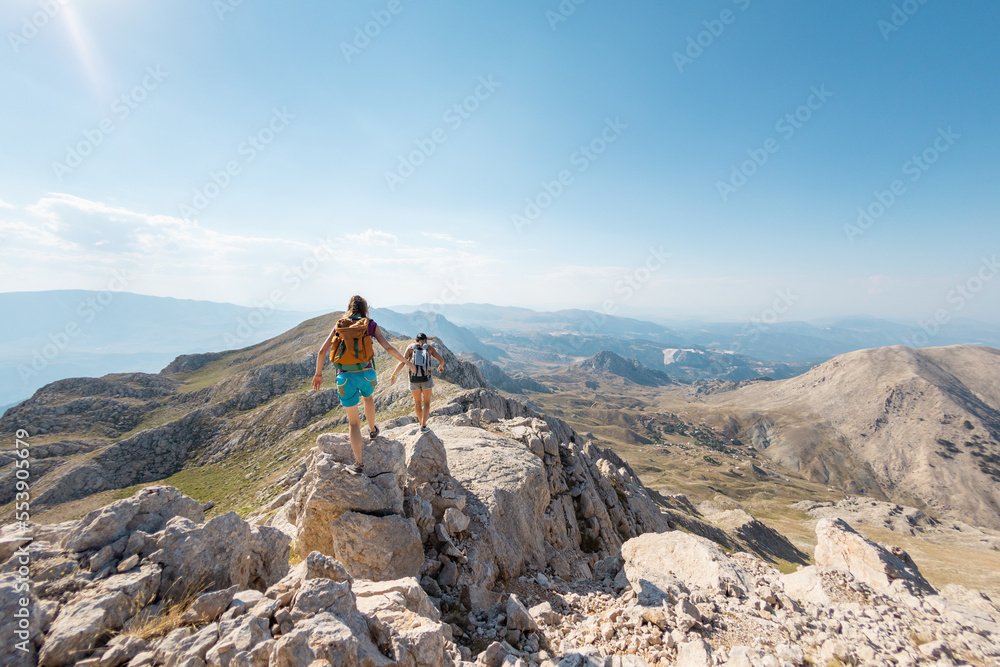 two girls with backpacks walk along a mountain path.