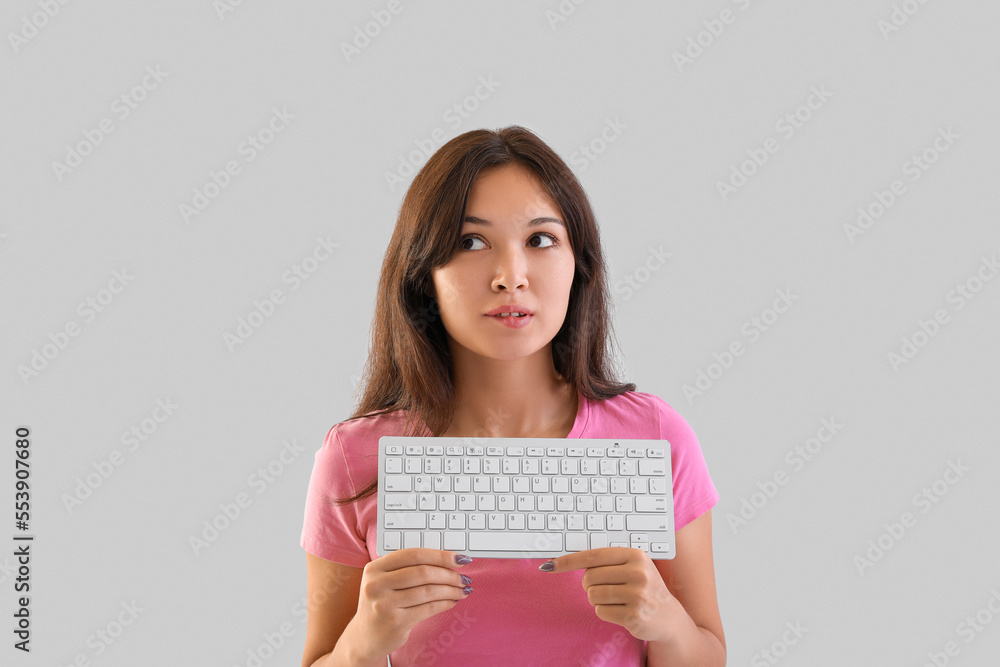 Thoughtful young Asian woman with computer keyboard on light background Thoughtful young Asian woman with computer keyboard on light background