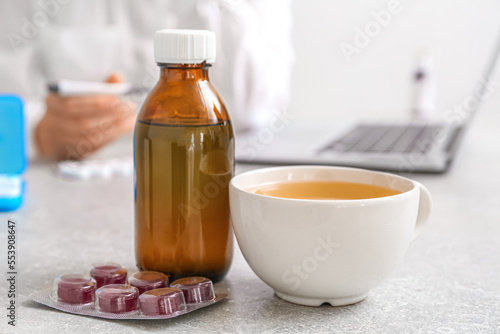 Cup of tea, pills for sore throat and cough syrup on table in office, closeup