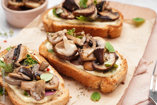 Wooden board of tasty toasts with cream cheese and mushrooms on light background, closeup