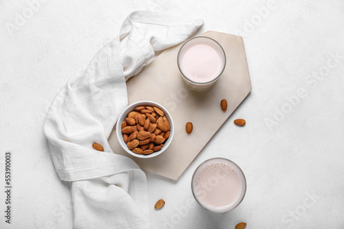 Board with glasses of healthy almond milk and nuts on light background
