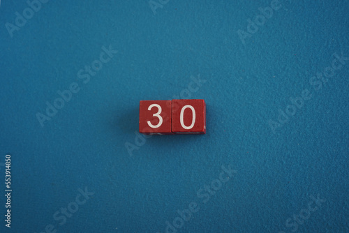 Wooden Viva Magenta cubes with number 30 blue background close-up top view. Concept of date or time. White numbers 30 on red cubes velvet background. Copy space for text or event. Blurred background