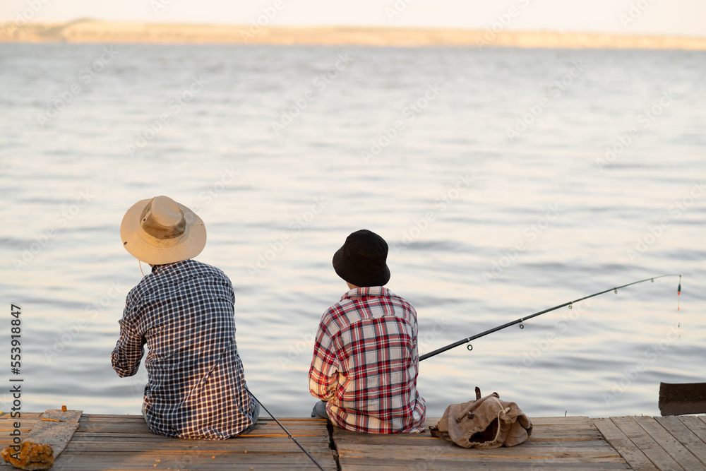 Back view teen son and father fishing in the summer on the pier Back view teen son and father fishing in the summer on the pier