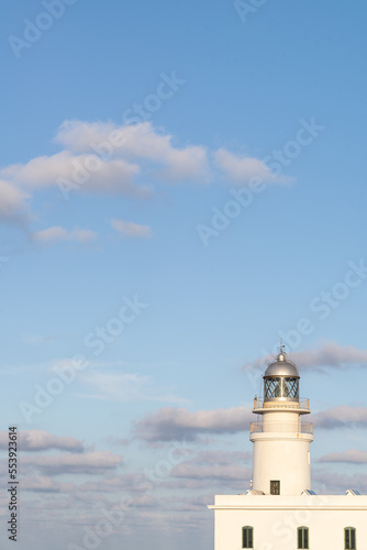 White ligthhouse with bue sky and some clouds at sunset located in Caballeria Cap  Menorca  Spain