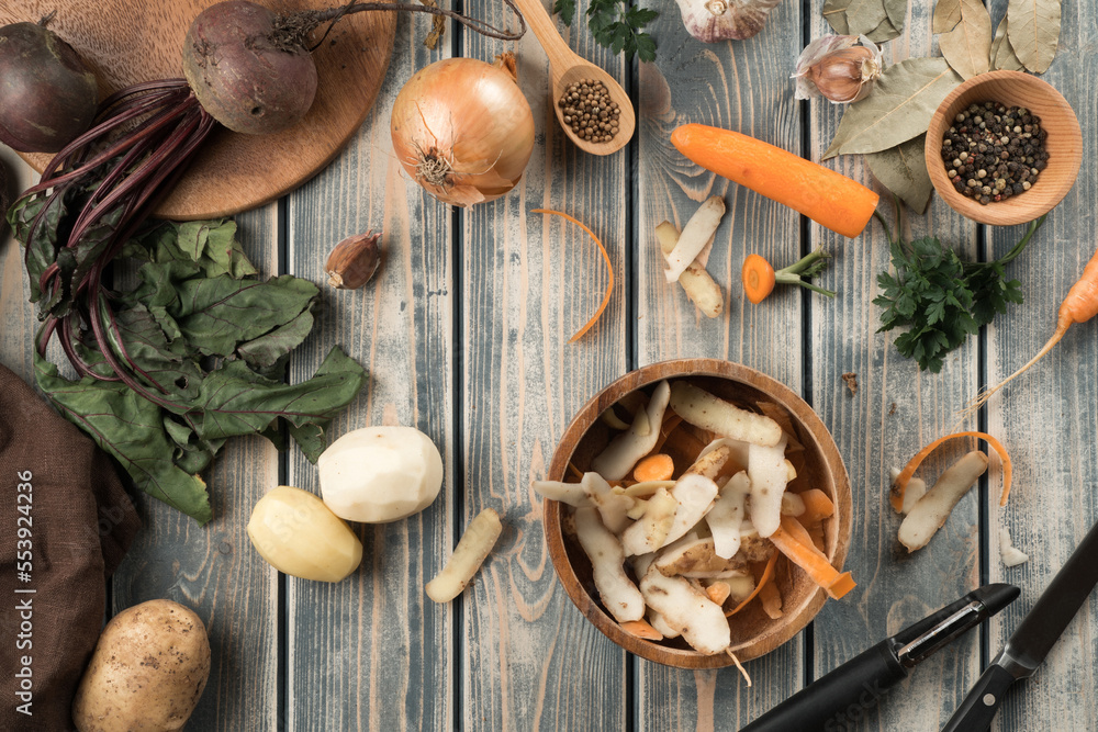 Composition of brown wooden bowl with potato peelings, little bowl with peppercorns, peeled potatoes, carrot, onion. Composition of brown wooden bowl with potato peelings, little bowl with peppercorns, peeled potatoes, carrot, onion.