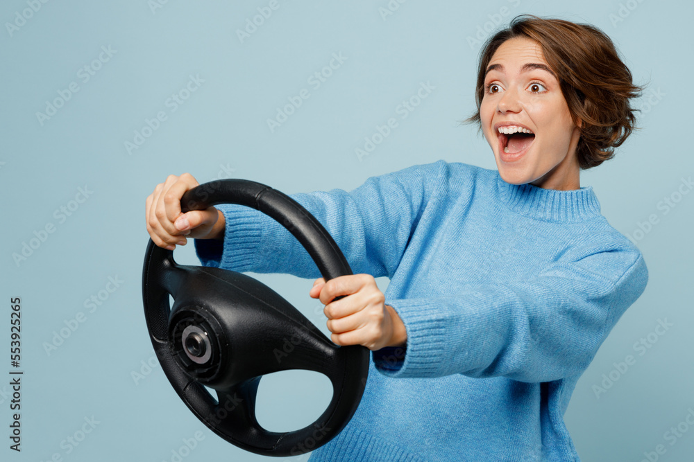 Side view young excited cheerful fun woman in knitted sweater look camera hold steering wheel driving car isolated on plain pastel light blue cyan background studio portrait People lifestyle concept Side view young excited cheerful fun woman in knitted sweater look camera hold steering wheel driving car isolated on plain pastel light blue cyan background studio portrait People lifestyle concept