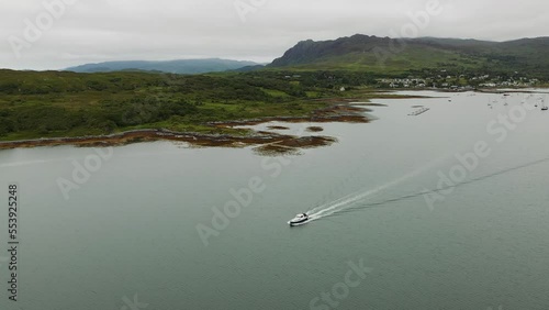 Cinematic aerial angle panning around boat cruising away from Arisaig Harbour on the West Coast of Scotland photo