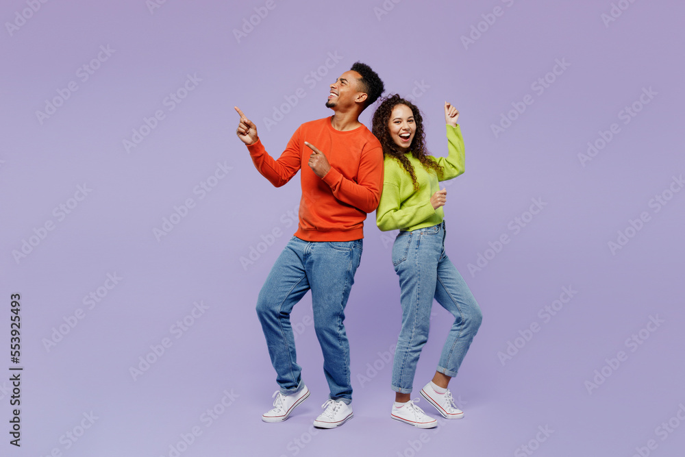 Full body sideways fun young couple two friends family man woman of African American ethnicity wear casual clothes together point finger aside on area isolated on pastel plain light purple background.
