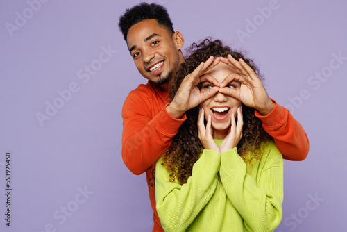 Young couple two friend family man woman of African American ethnicity in casual clothes together hold hand near eyes imitating glasses or binoculars isolated on pastel plain light purple background