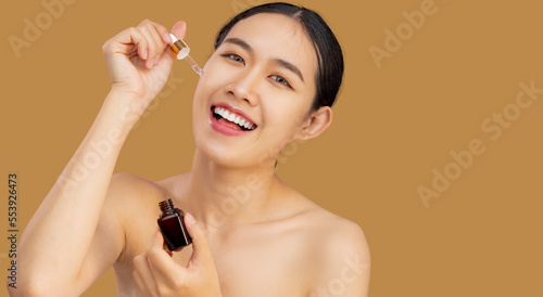 Beautiful asian woman dropping essential oil for skin care, applying serum on clean face for treatment .