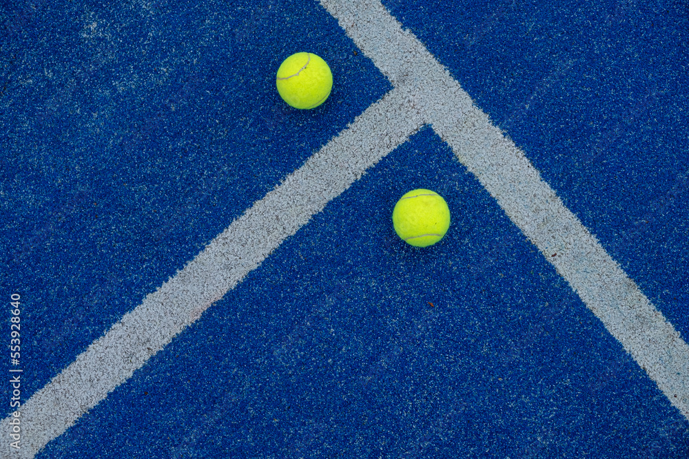 two tennis balls on a blue turf court paddle tennis court