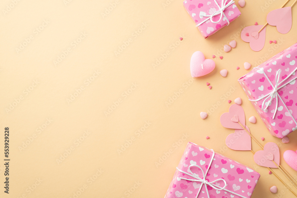 Valentine's Day concept. Top view photo of pink gift boxes paper hearts on sticks candle and sprinkles on isolated beige background with copyspace