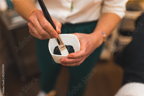 closeup view of cosmetologist's hands holding a small jar with facial mask and putting a brush in it, spa concept. High quality photo