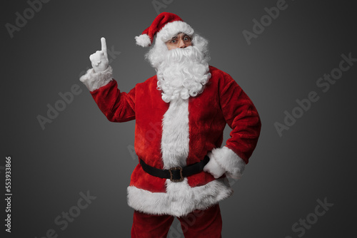 Portrait of old santa claus dressed in red suit pointing up.