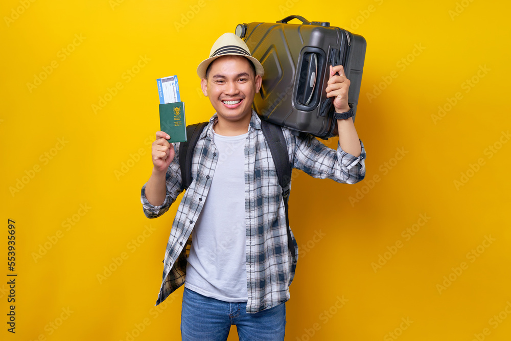 Traveler fun tourist Asian man in casual clothes hat with backpack holding suitcase and passport ticket on yellow background. Passenger travel abroad on weekend getaway Air flight journey concept Traveler fun tourist Asian man in casual clothes hat with backpack holding suitcase and passport ticket on yellow background. Passenger travel abroad on weekend getaway Air flight journey concept