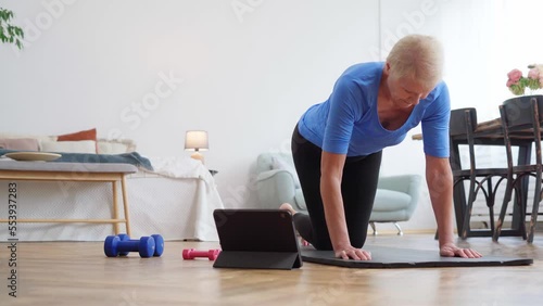 elderly woman doing exercises with an online trainer in her living room.
