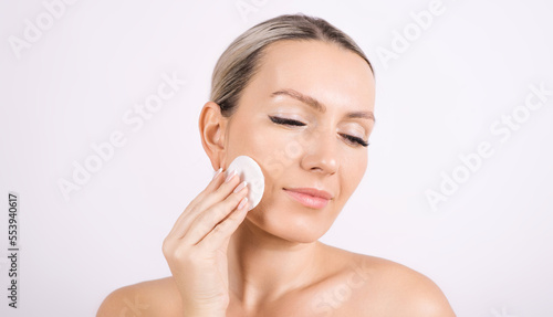 A woman cleans her face, removes makeup with a cotton pad on a white background.