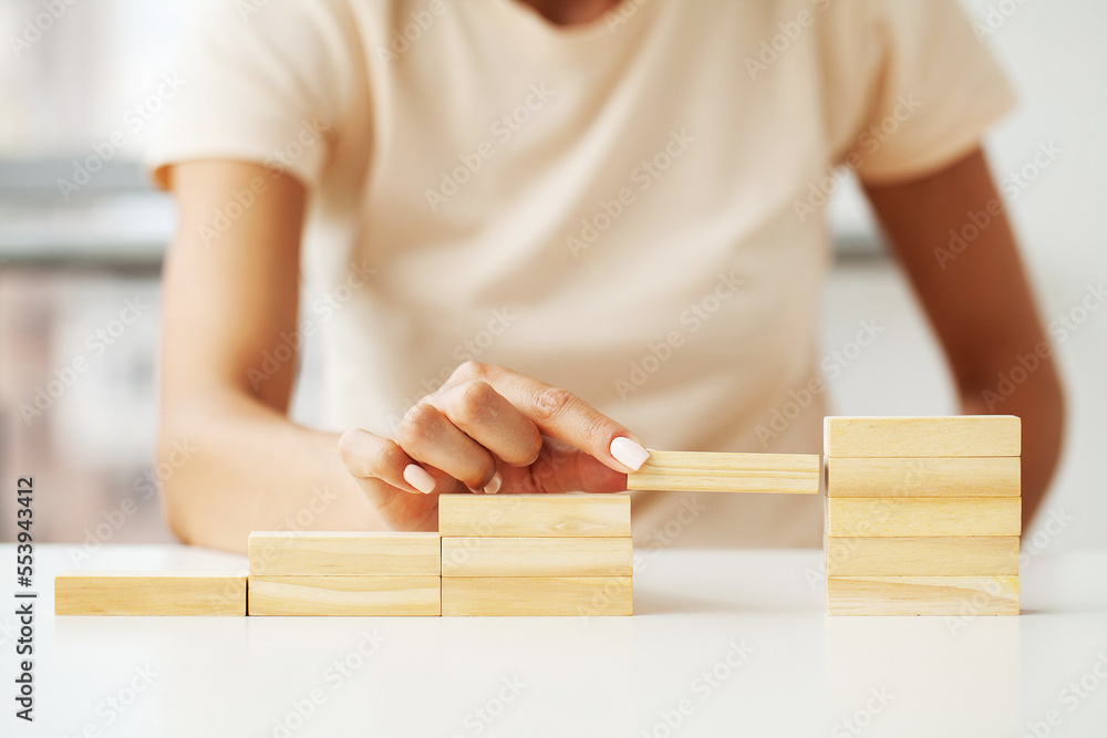Woman hand arranging wood cube stacking as stair step shape
