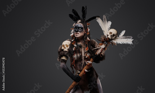 Shot of fearful necromancer with fur holding staff against grey background.