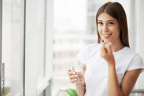Fotografia, Obraz Young woman takes round pill with glass of water in hand